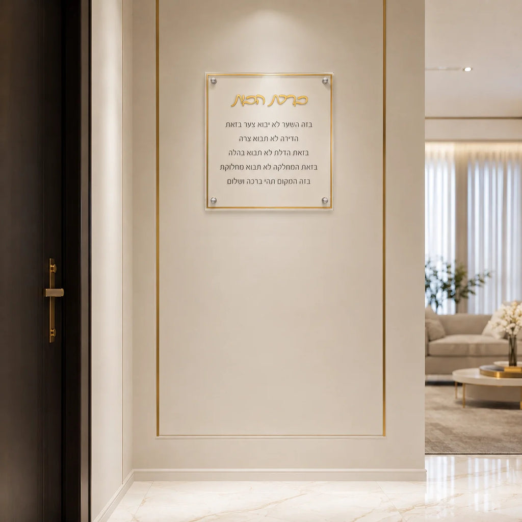 A modern interior hallway with a rectangular gold-framed glass plaque mounted on a cream wall. The plaque features Hebrew text in gold and black, and the surrounding space includes a dark wood door on the left and a softly lit living room in the background.