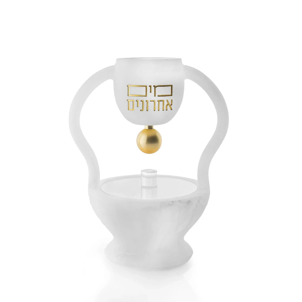 A cup suspended in a curved arch above a covered footed bowl, in marbled resin with raised gold Hebrew lettering. In marble.
