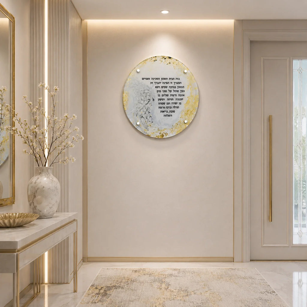 A round decorative wall art piece with gold and white marbled accents and black Hebrew text, mounted on a beige wall in a modern, elegant hallway with a console table and vase.