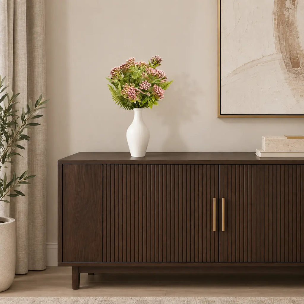 Tall white ceramic vase with pink faux flowers styled on a dark fluted sideboard beside a framed canvas