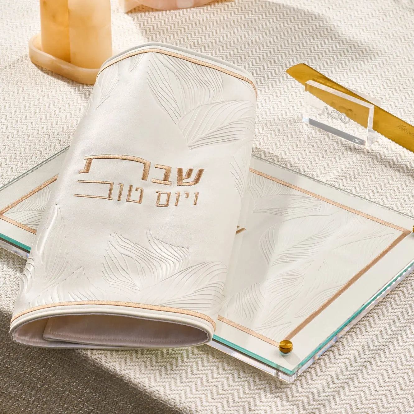 Embossed leaf challah board in cream leather with gold accents, displayed with shabbat items on a neutral surface