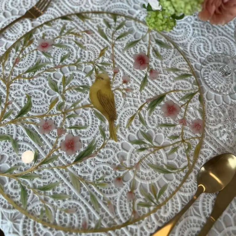 Floral bird charger with yellow songbird, delicate pink flowers, and green foliage on white lace background with gold rim.