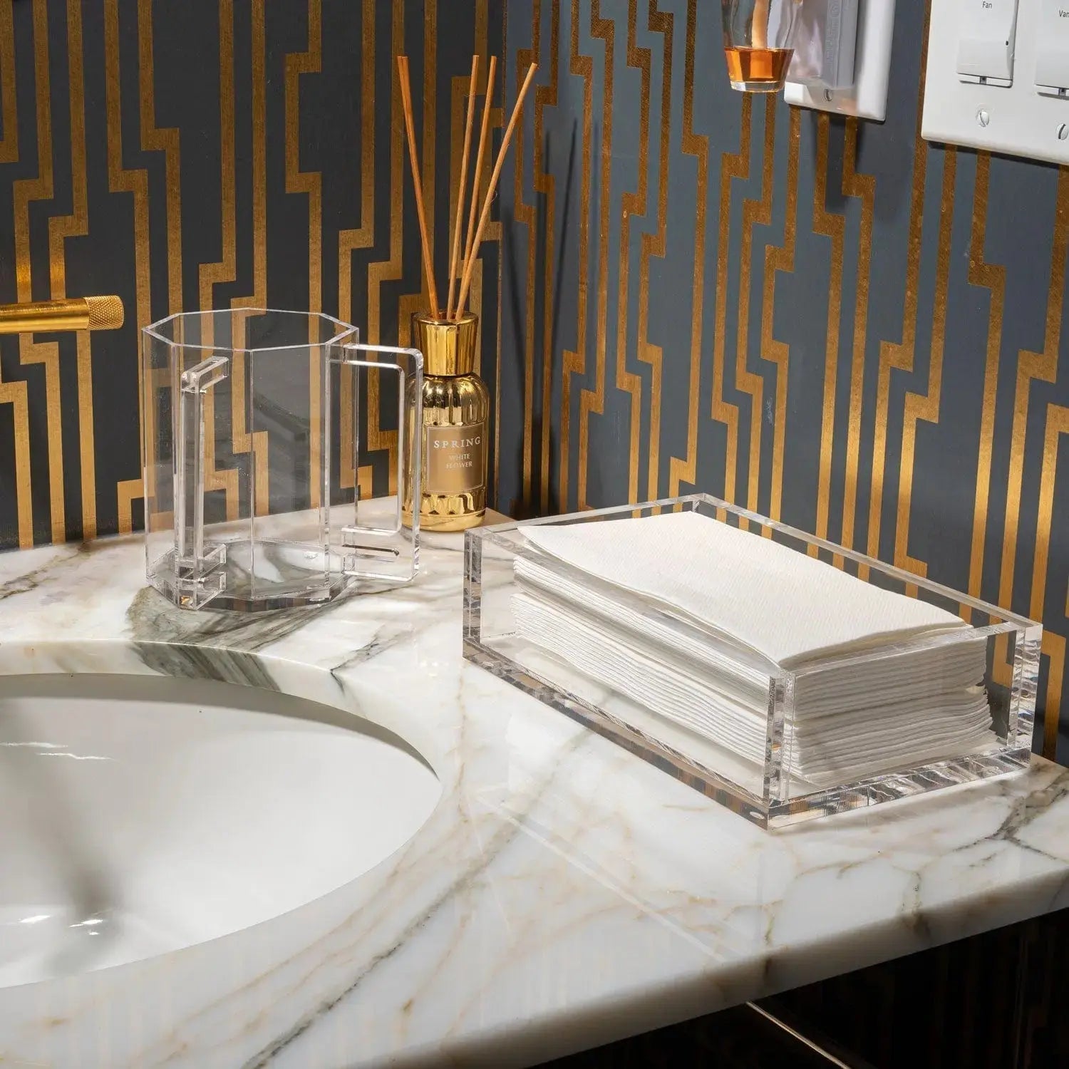 Marble hexagon washing cup by Waterdale Collection displayed on a bathroom vanity with gold accessories and white sink.