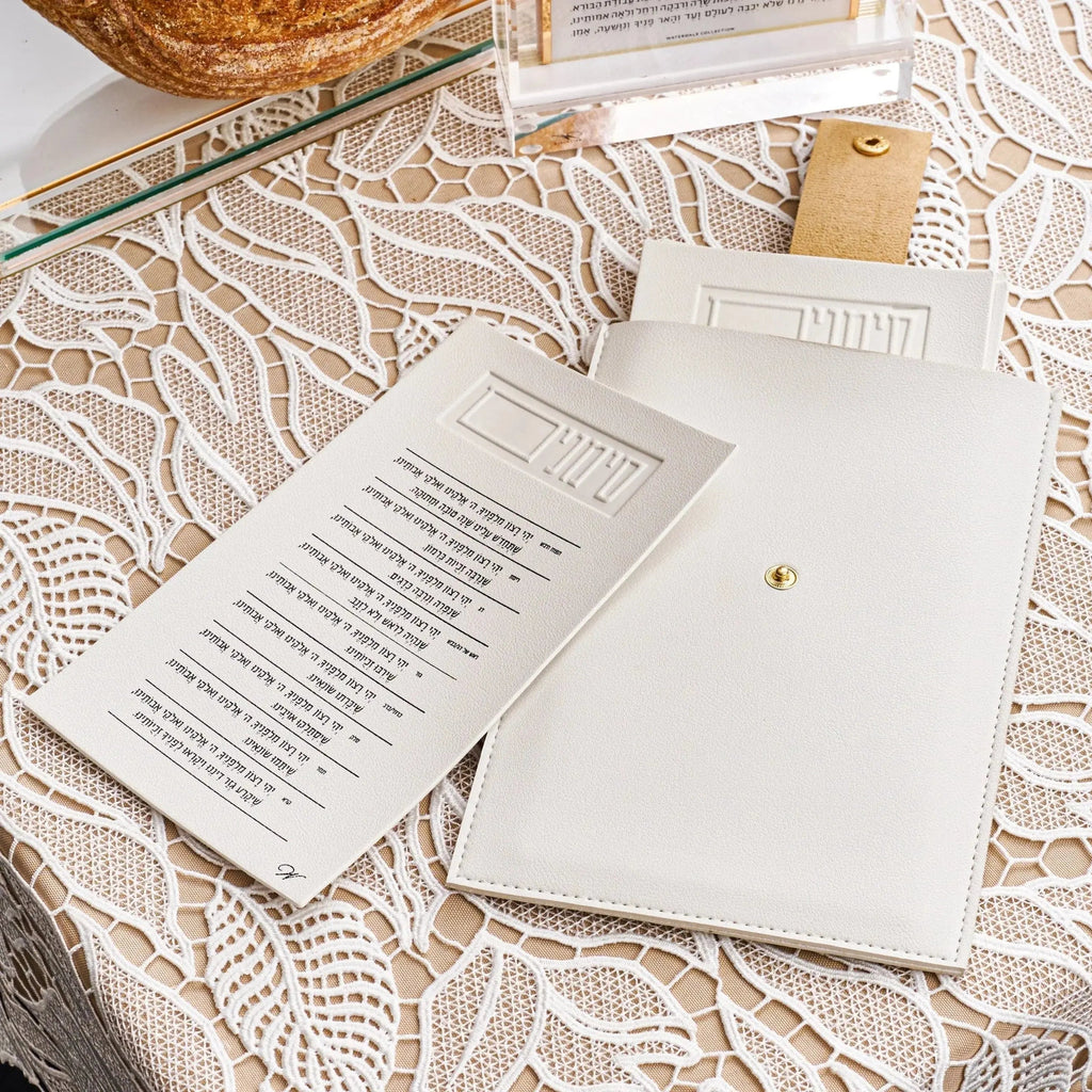 Leather Simanim pouch in tan with white lucite cards displayed on patterned fabric, showing product packaging and contents for Rosh Hashanah.