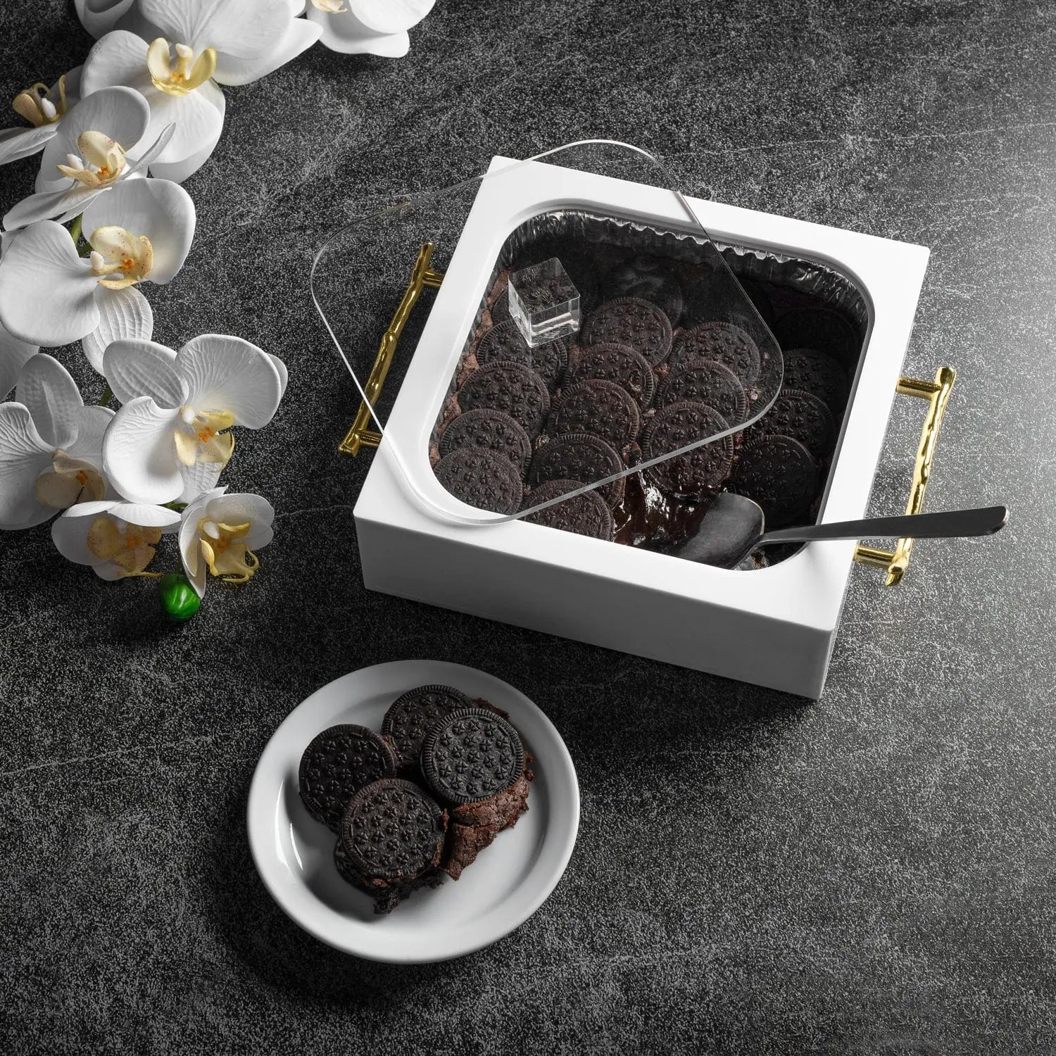 White ceramic 8x8 pan holder by Waterdale Collection with dark serving dish, styled with white orchids and gray surface