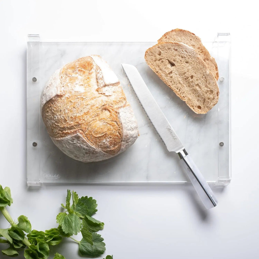 Waterdale Collection bread knife with serrated blade cutting through crusty artisan bread on marble board with herbs nearby