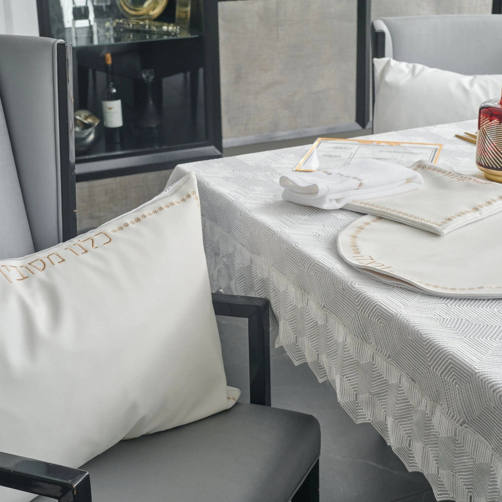 Inspired Leather Pesach Set in white and gold displayed on a dining table with place settings and linens, showcasing the elegant tabletop collection.