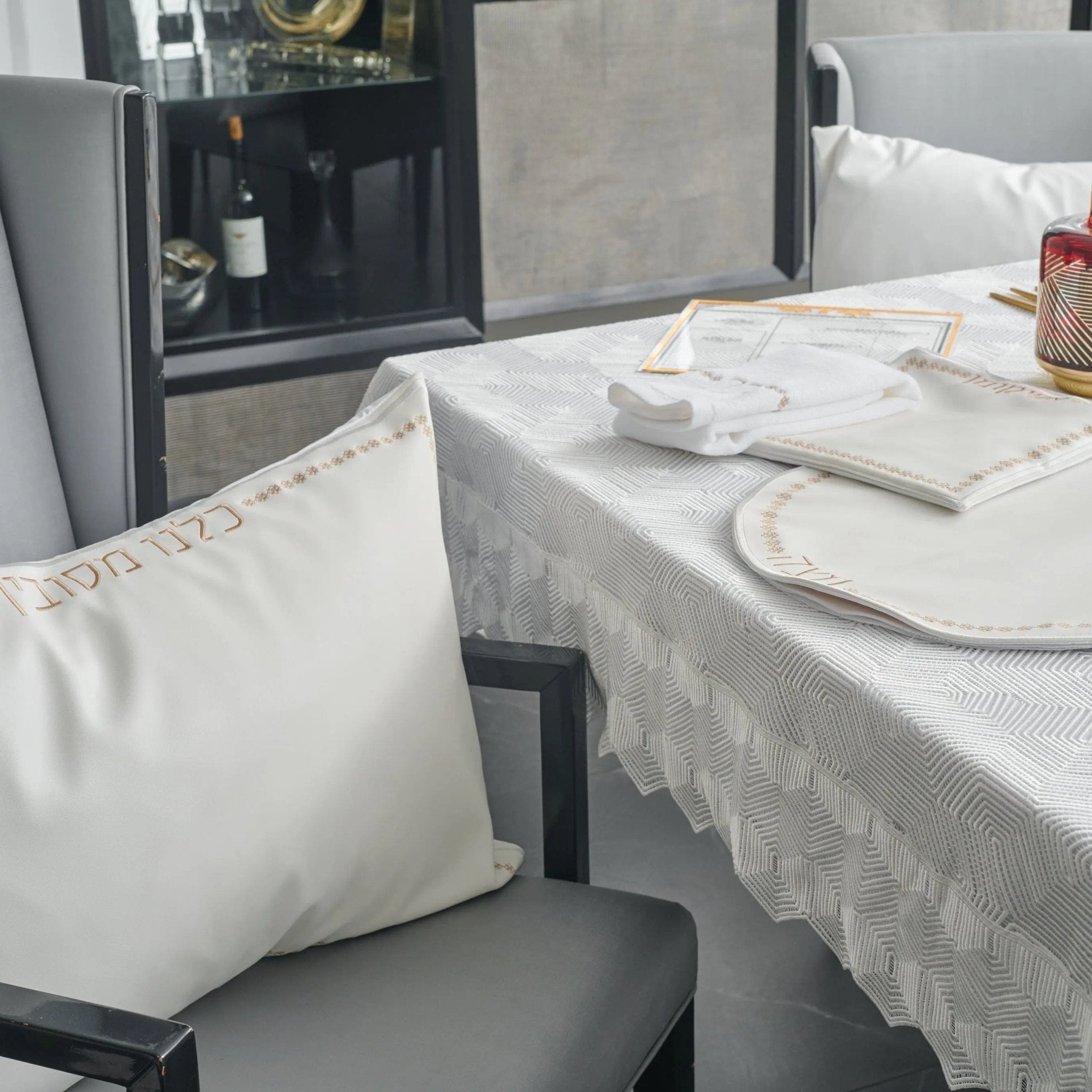 Inspired Leather Pesach Set in white and gold displayed on a dining table with place settings and linens, showcasing the elegant tabletop collection.