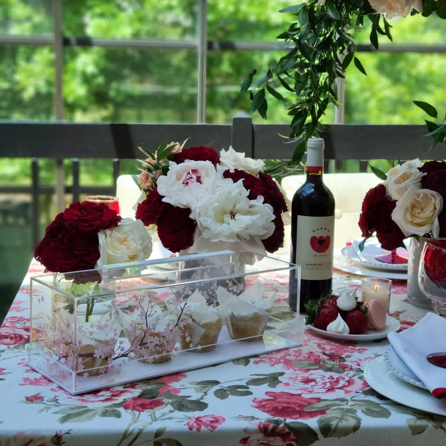 Clear glass Cherry Blossom cake dome with red floral design, displayed on an elegant table setting with flowers and place settings.