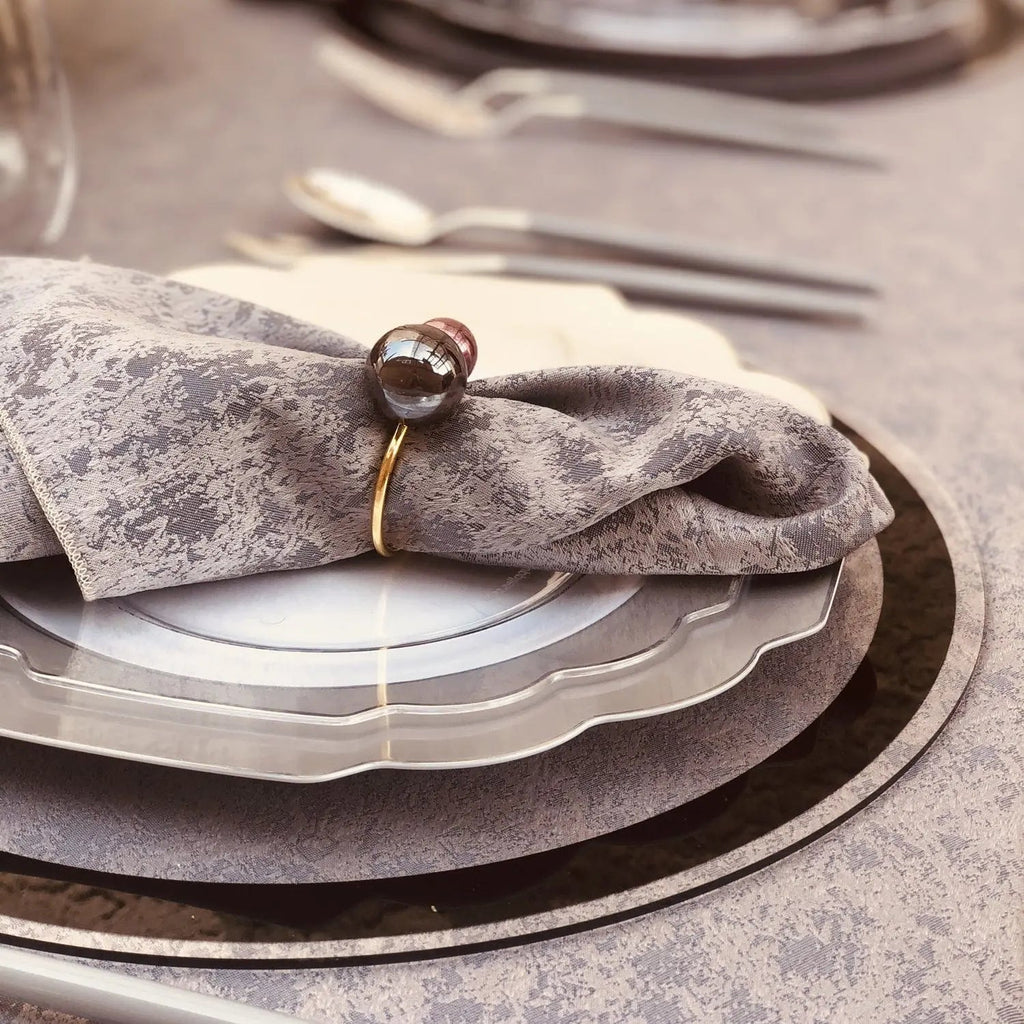 Classic Chargers in silver with black border, layered on plates with folded linen napkin and gold napkin ring for elegant table setting.