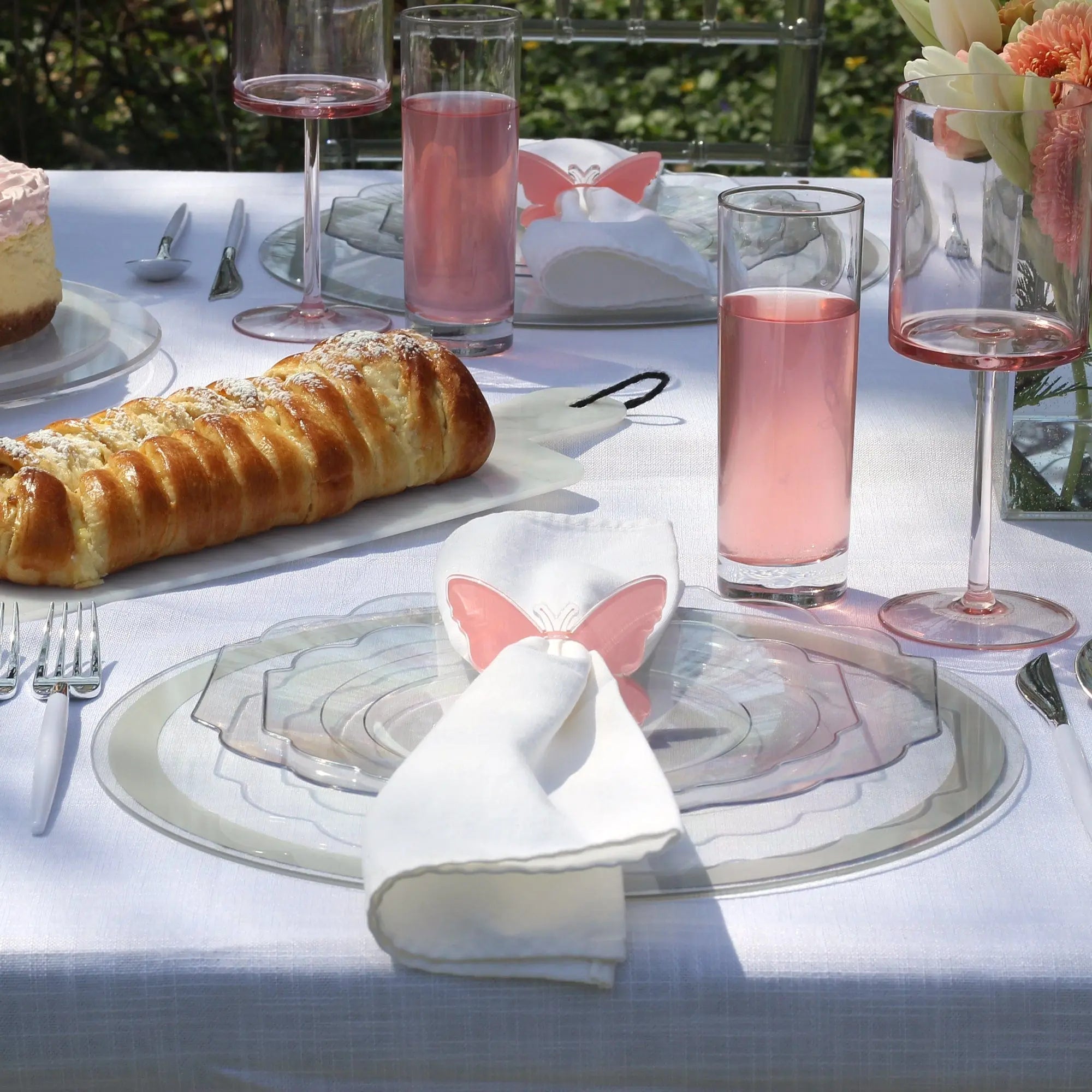 Silver-bordered Classic Charger plate with white napkin and pink bow at formal place setting with bread and pink beverages.