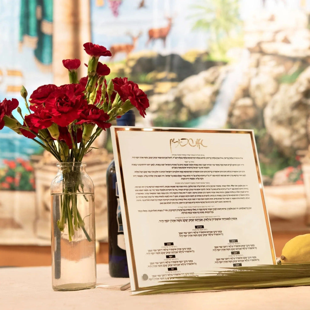 Classic Tabletop Ushpizin plaque displayed with red flowers in glass vase, showing Hebrew text and artwork on white card stand for Sukkot holiday decor.