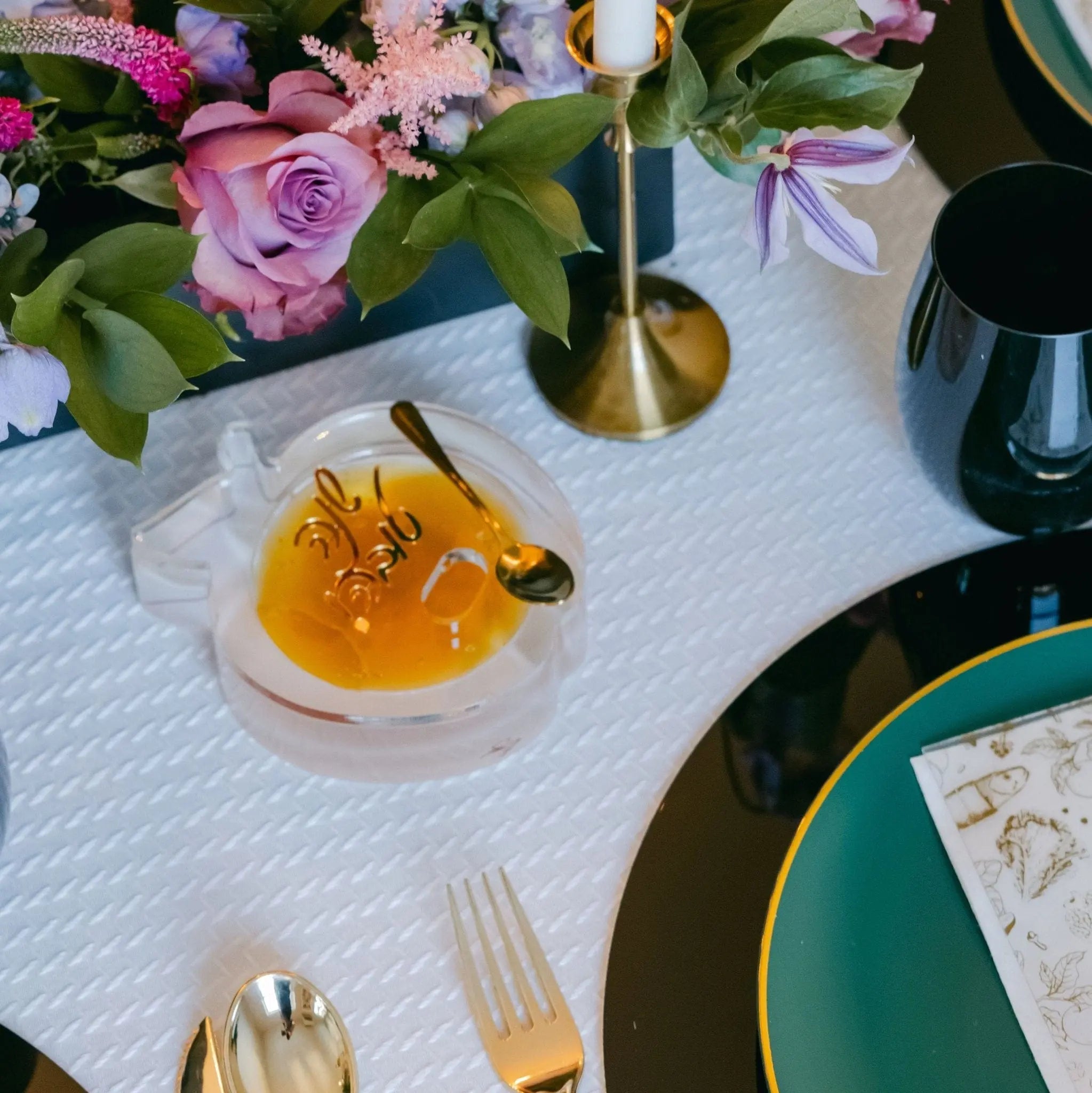 Golden die-cut apple honey dish by Waterdale Collection displayed on white tablecloth with table setting and flowers.
