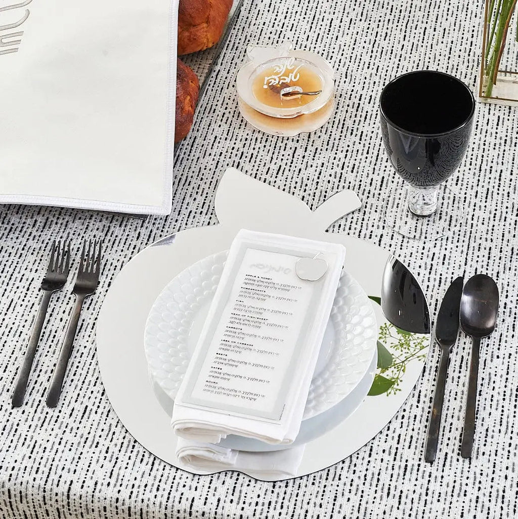 Die-cut apple-shaped honey dish in white ceramic displayed on a formal place setting with black utensils