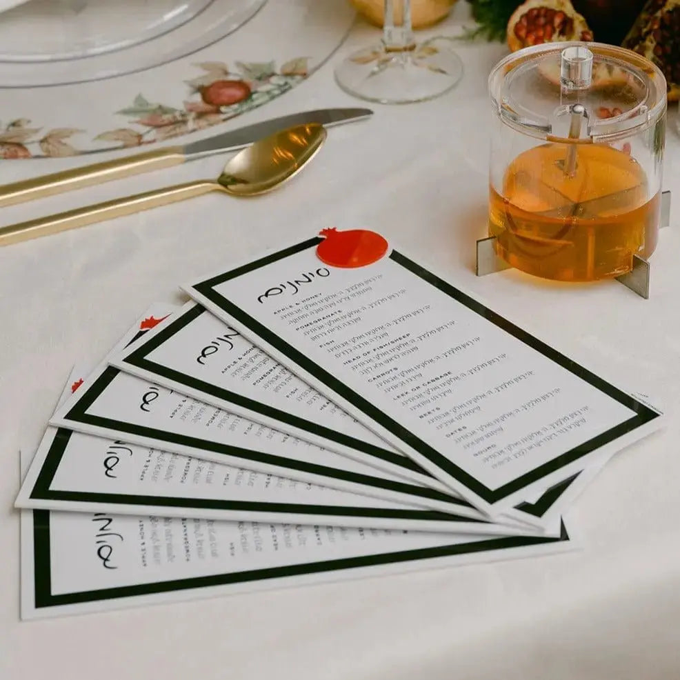 Die-cut pomegranate lucite Simanim card displayed with holiday table setting and wine glass, Rosh Hashanah greeting card