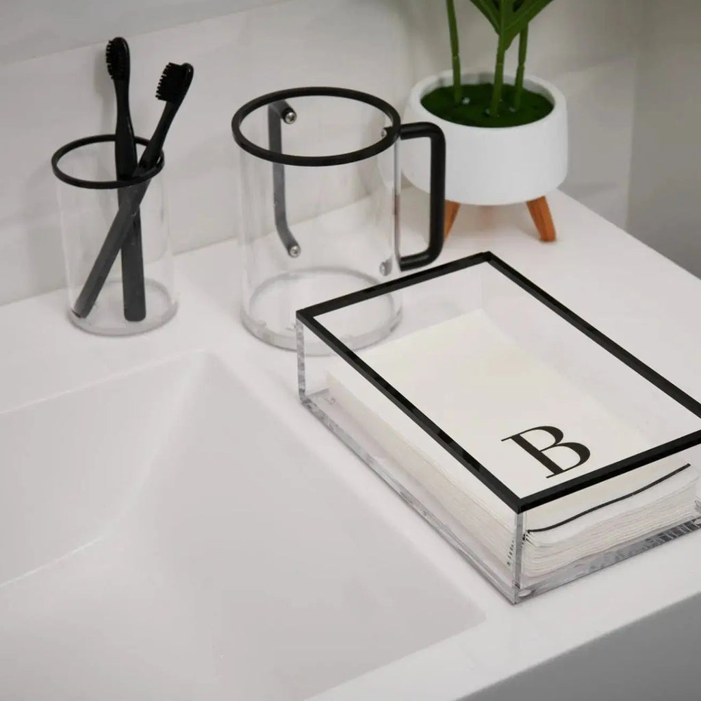 Edge Washing Cup in clear glass with black geometric trim, displayed on white vanity with bathroom accessories and plant.