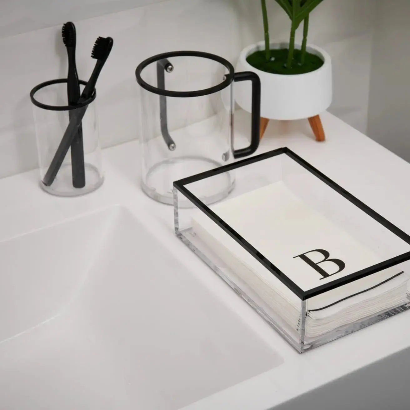 Edge Washing Cup in clear glass with black geometric trim, displayed on white vanity with bathroom accessories and plant.