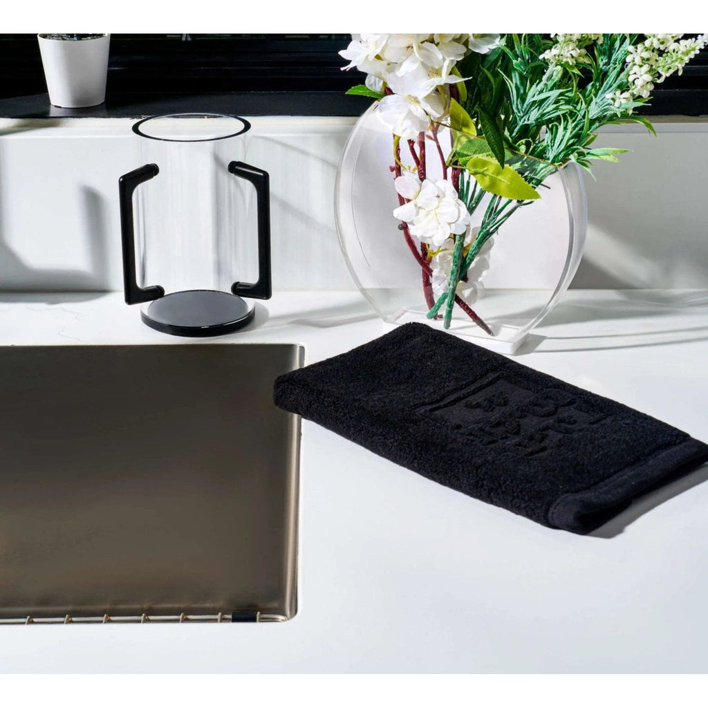 Black Edge washing cup with curved handles displayed on white counter next to clear vase with white flowers and bathroom accessories
