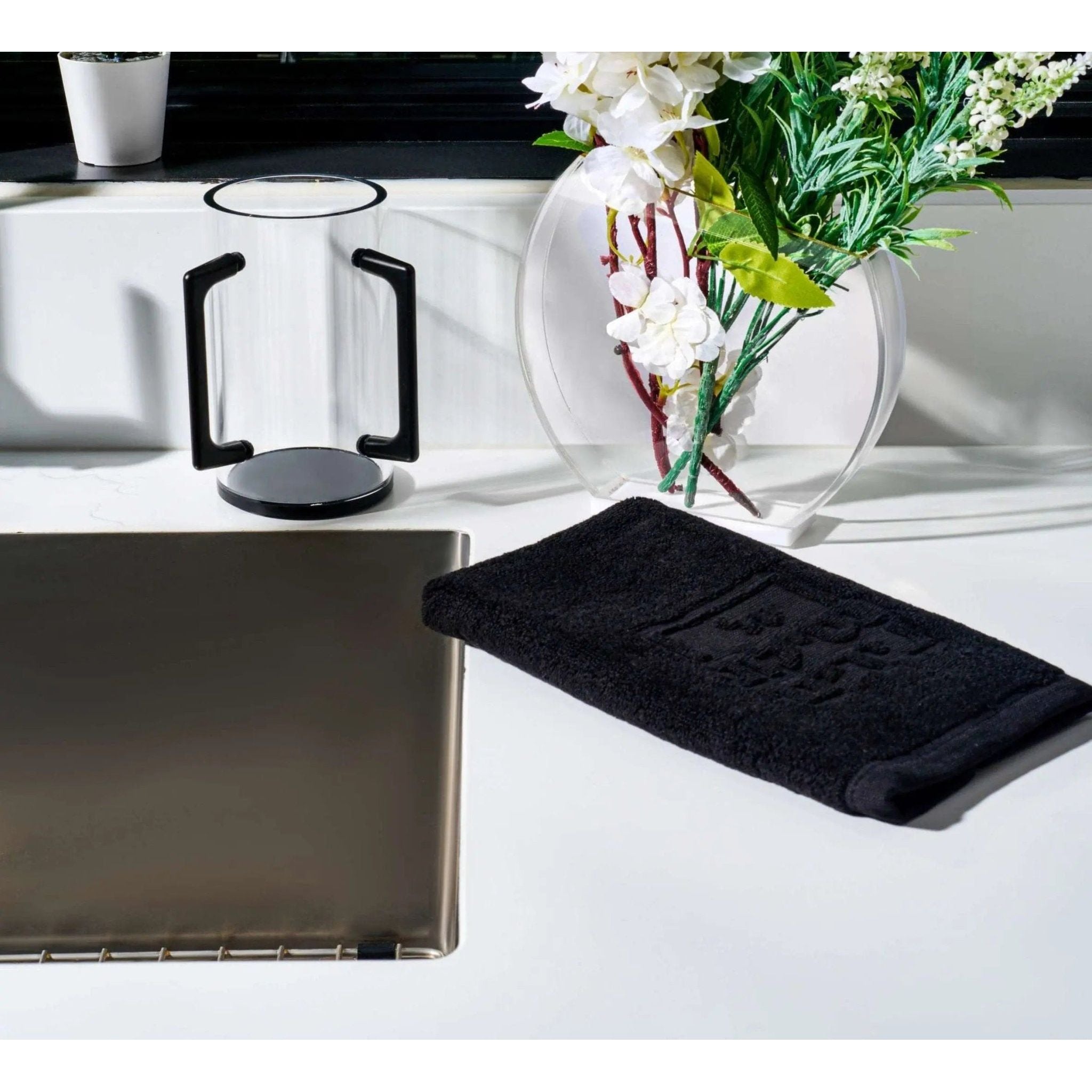 Black Edge washing cup with curved handles displayed on white counter next to clear vase with white flowers and bathroom accessories