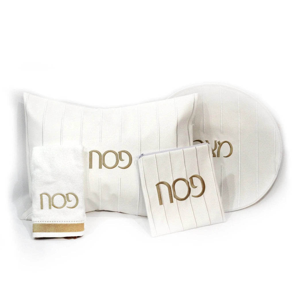 Embroidered Pesach set with cream pillows, matching plate, and napkins featuring gold "noo" lettering on leather tabletop accents.