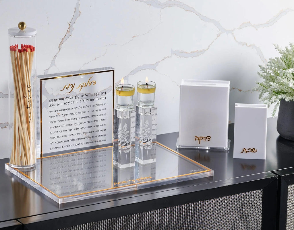 Pair of clear crystal candlesticks with engraved design displayed on black surface alongside candles and Shabbat items