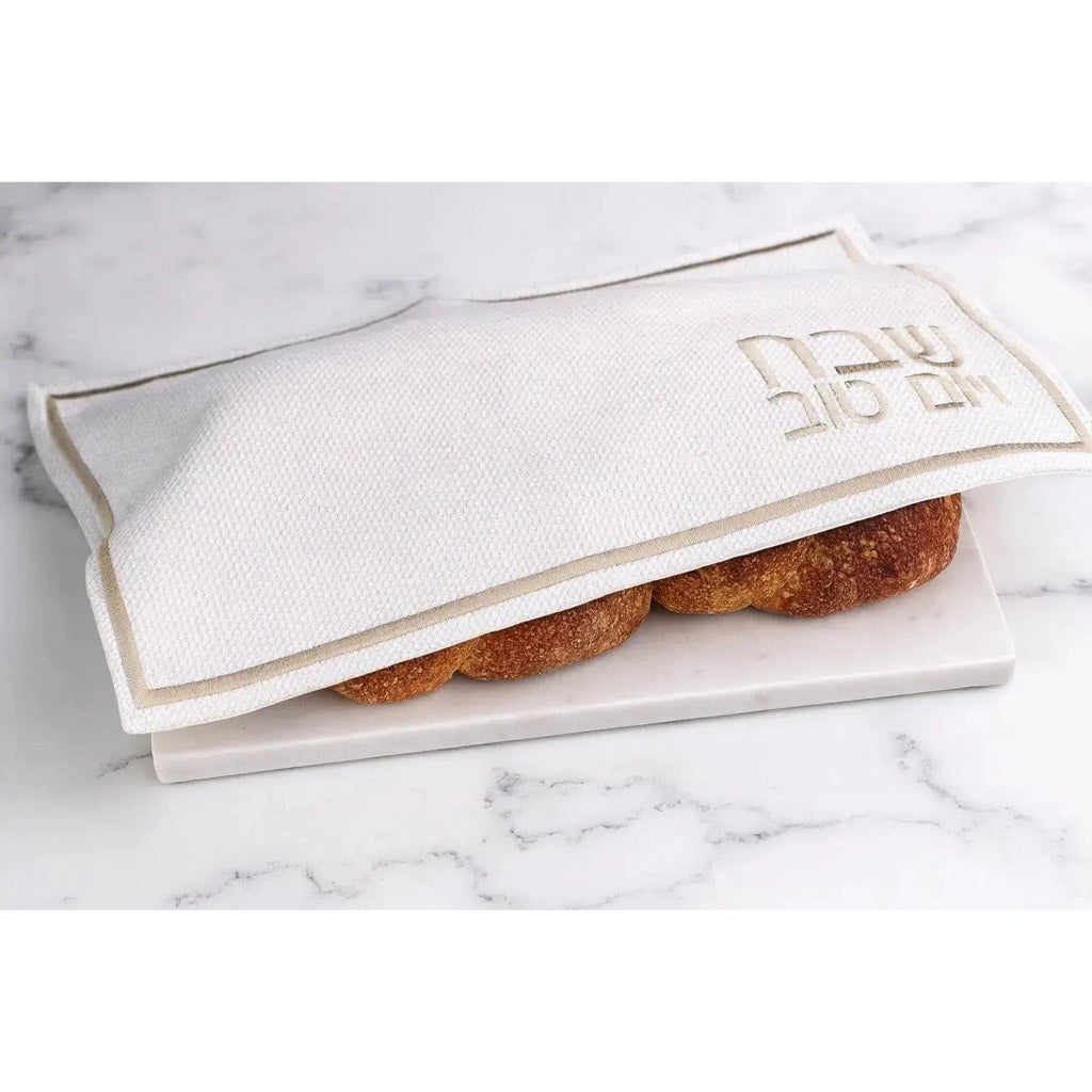 Cream and gold fabric challah cover with embroidered design, displayed open on marble surface with challah bread visible inside