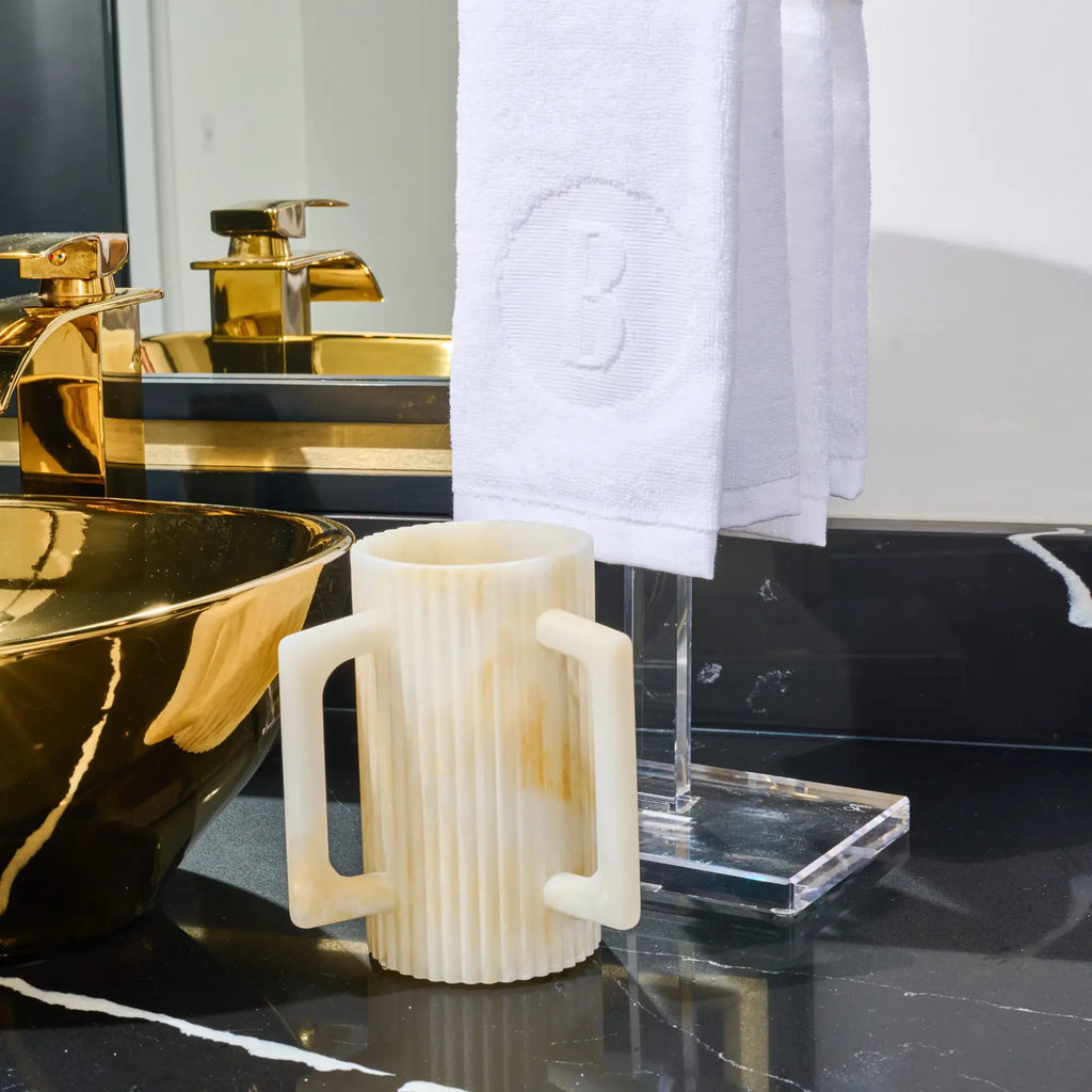 Fluted resin washing cup with two handles for Netilat Yadayim on bathroom counter.