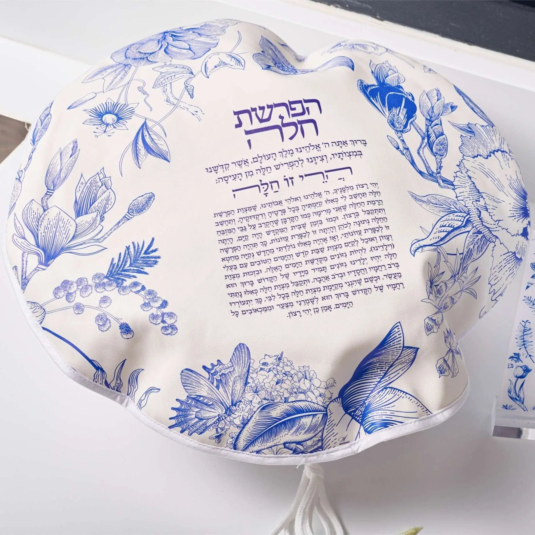 French Toile Hafrashas Challah Cover in white leather with blue floral design, featuring decorative tassels and Hebrew text for Shabbat.