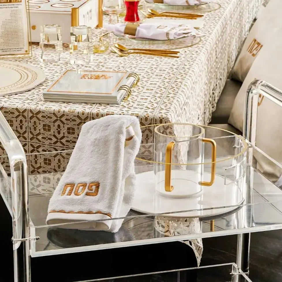 Metallic washing bowl and cup set in gold tone, displayed on a white stand with table settings and holiday dinnerware in background.