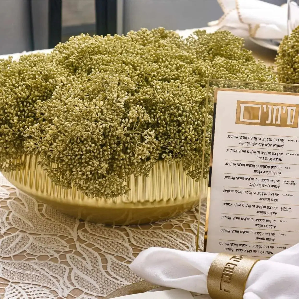 Greenery Gold Flower Pot with textured faux foliage in gold tones, displayed on white table linens with place setting.