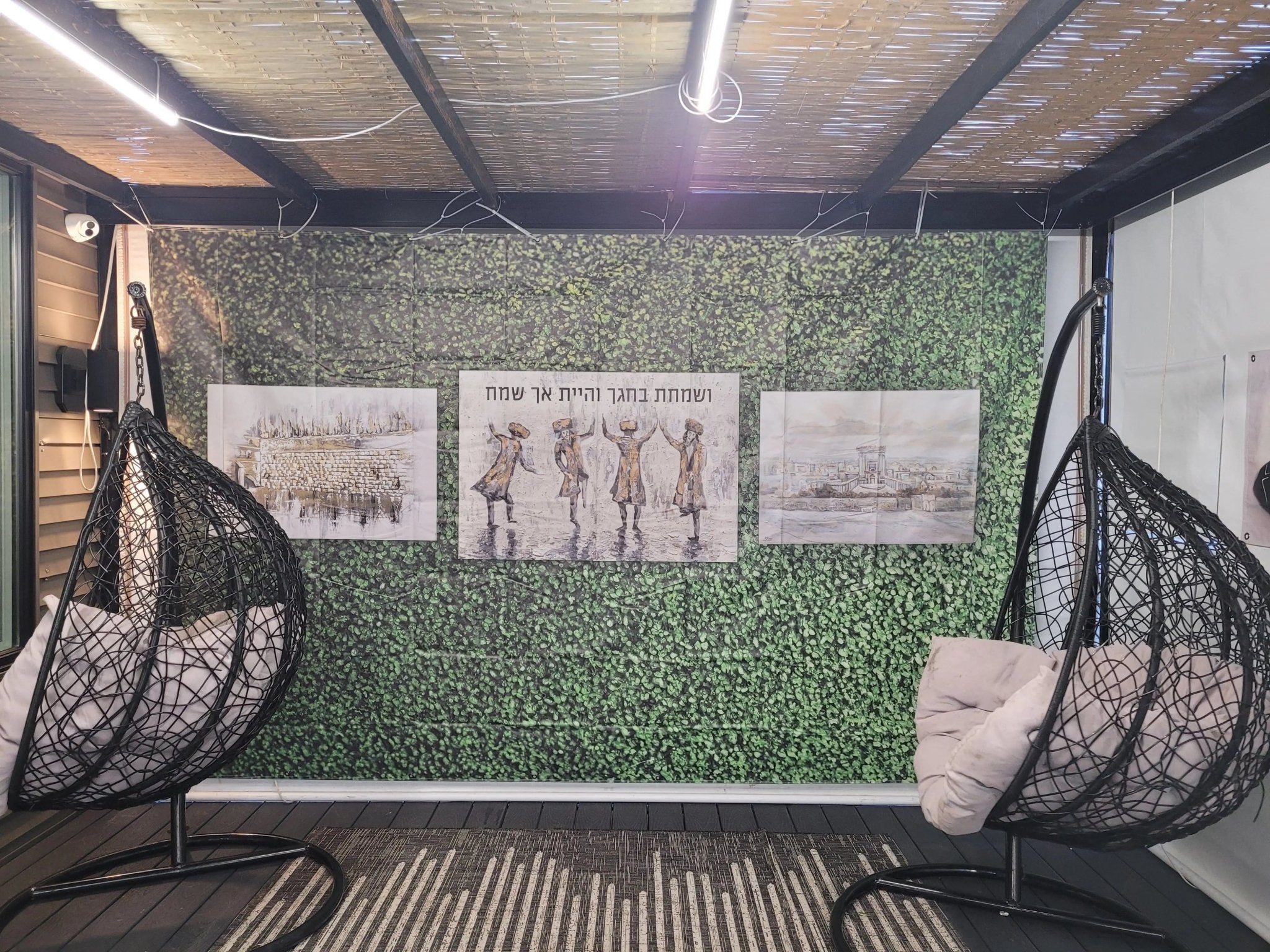 Painted by Batya greenery vinyl mural decorating a sukkah interior with hanging chairs and natural plant-themed wall art for Sukkot holiday.