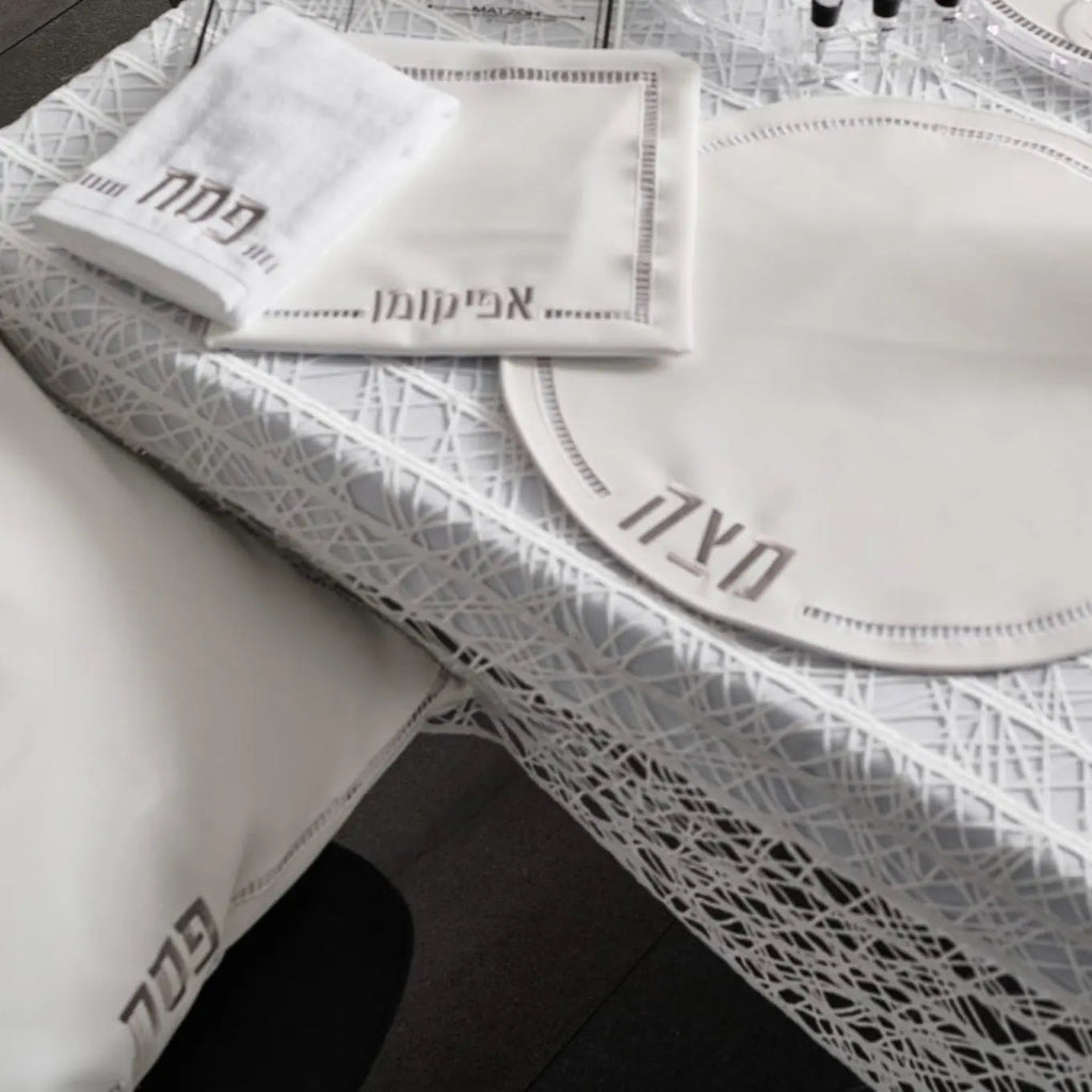 Hemstitched Pesach set with white linen napkins and gray fabric trim, featuring delicate embroidered details and leather accents.