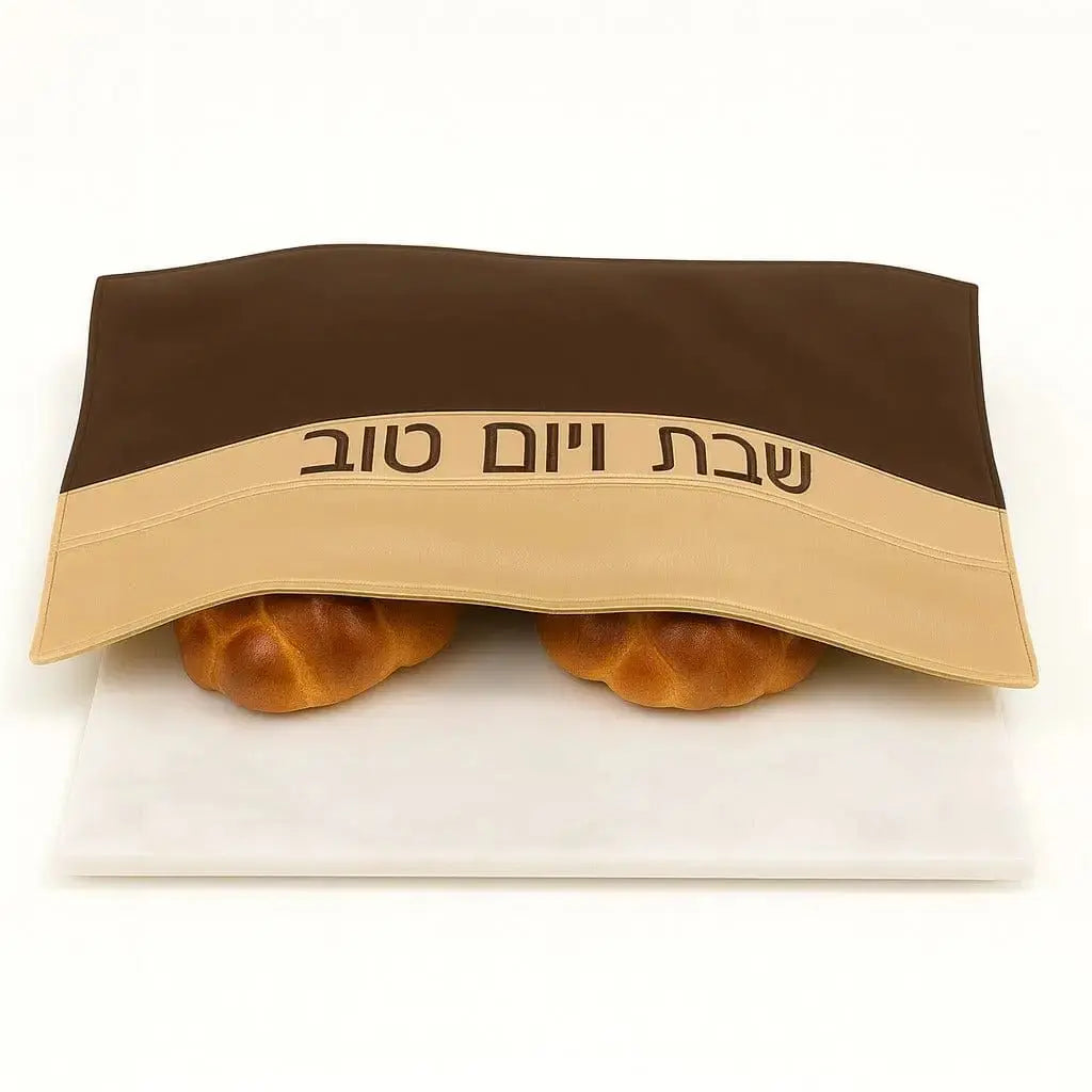 Brown and tan leather challah cover with Hebrew text, displaying two braided loaves of bread underneath for Shabbat.