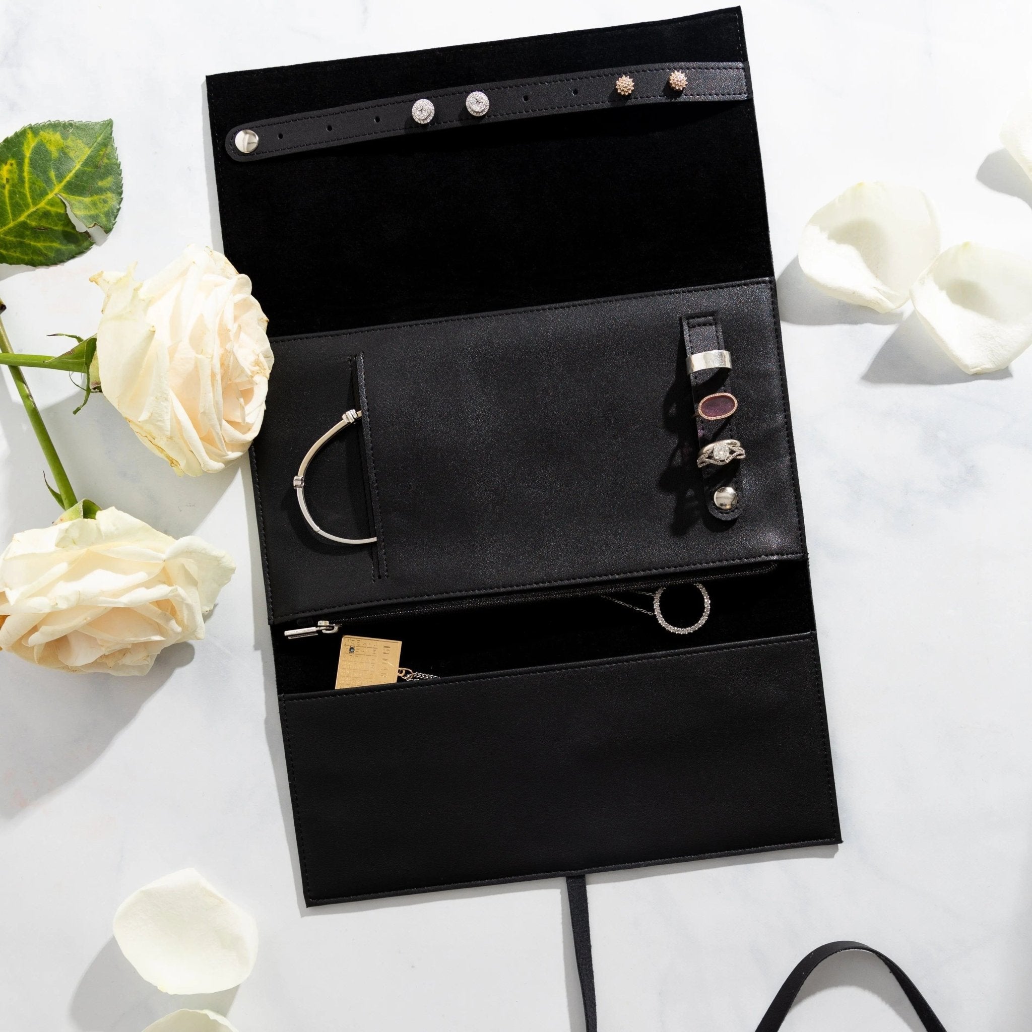 Black leather jewelry roll organizer with multiple compartments displaying rings, necklaces, and bracelets from Waterdale Collection.