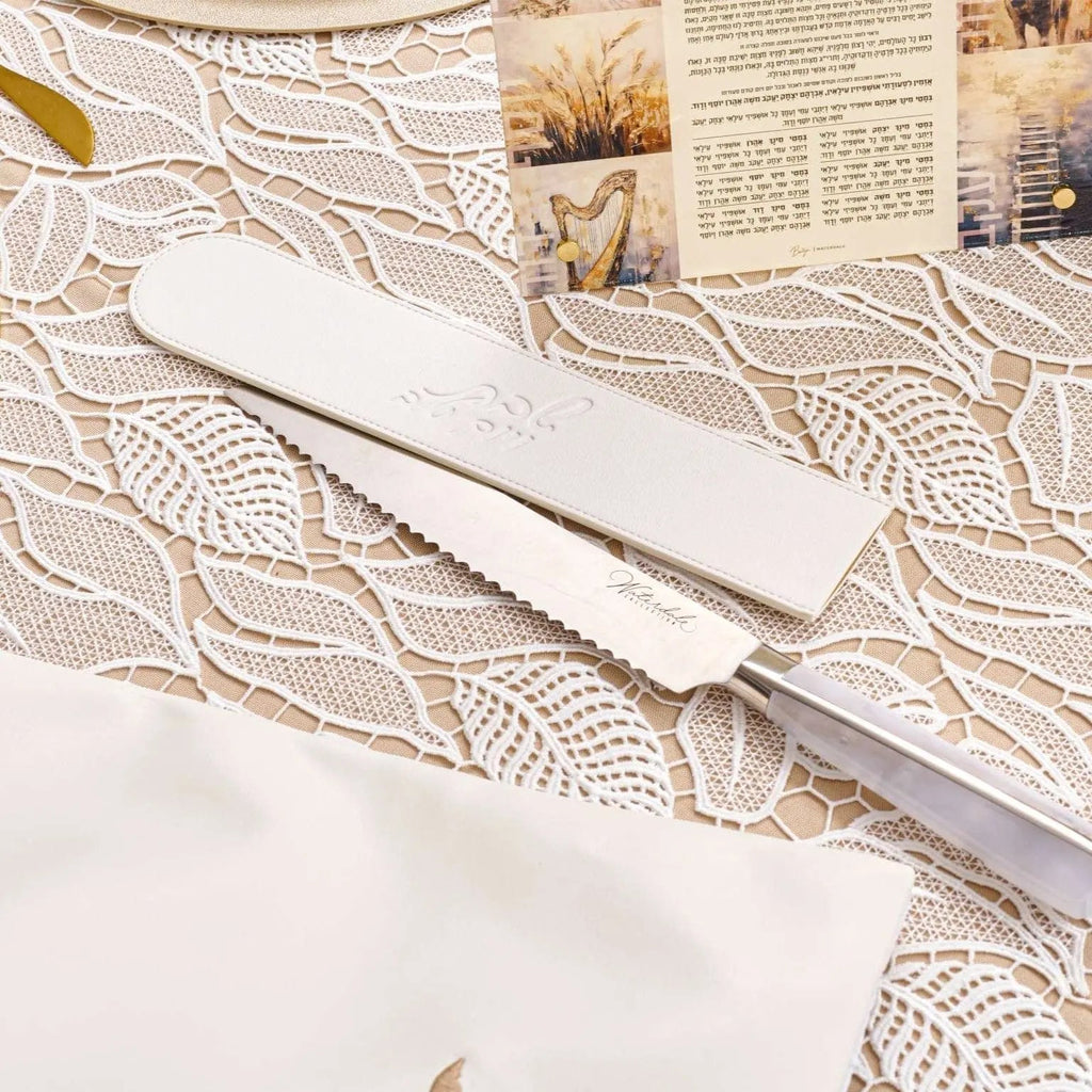 Cream leather knife blade cover displayed on a patterned challah board with dried flowers and newspaper in background.
