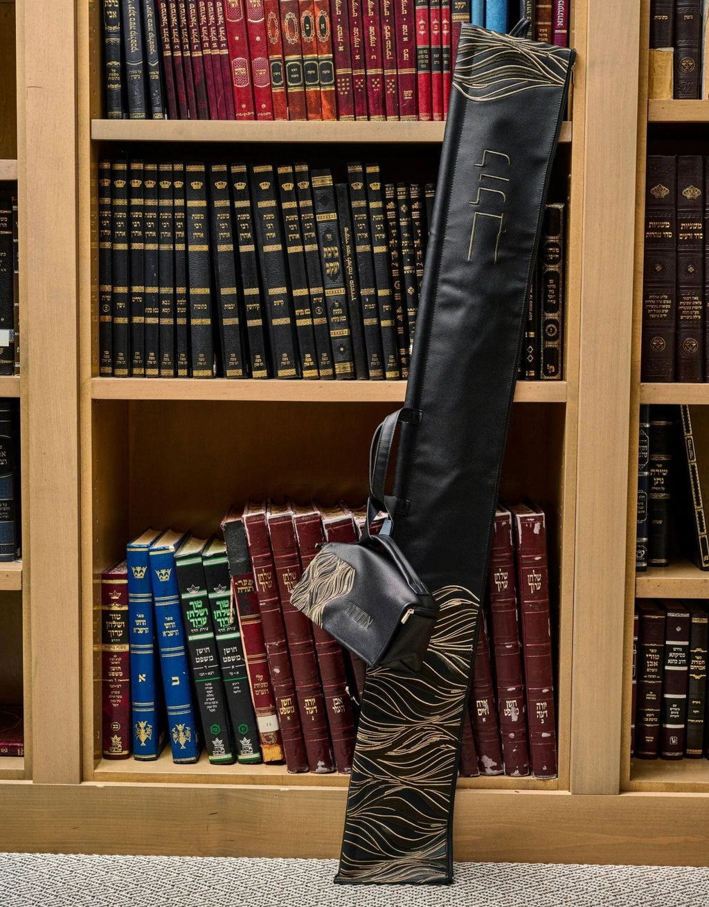 Black leather lace lulav case displayed upright against a bookshelf backdrop, showing ornate lattice pattern detailing and rich texture.