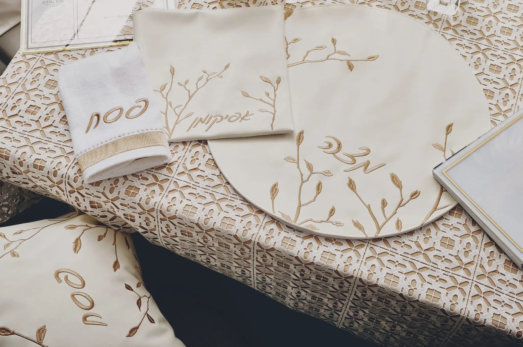 Leaf Pesach Set in gold and white leather with delicate botanical leaf design on cream tableware, displayed on natural linen.