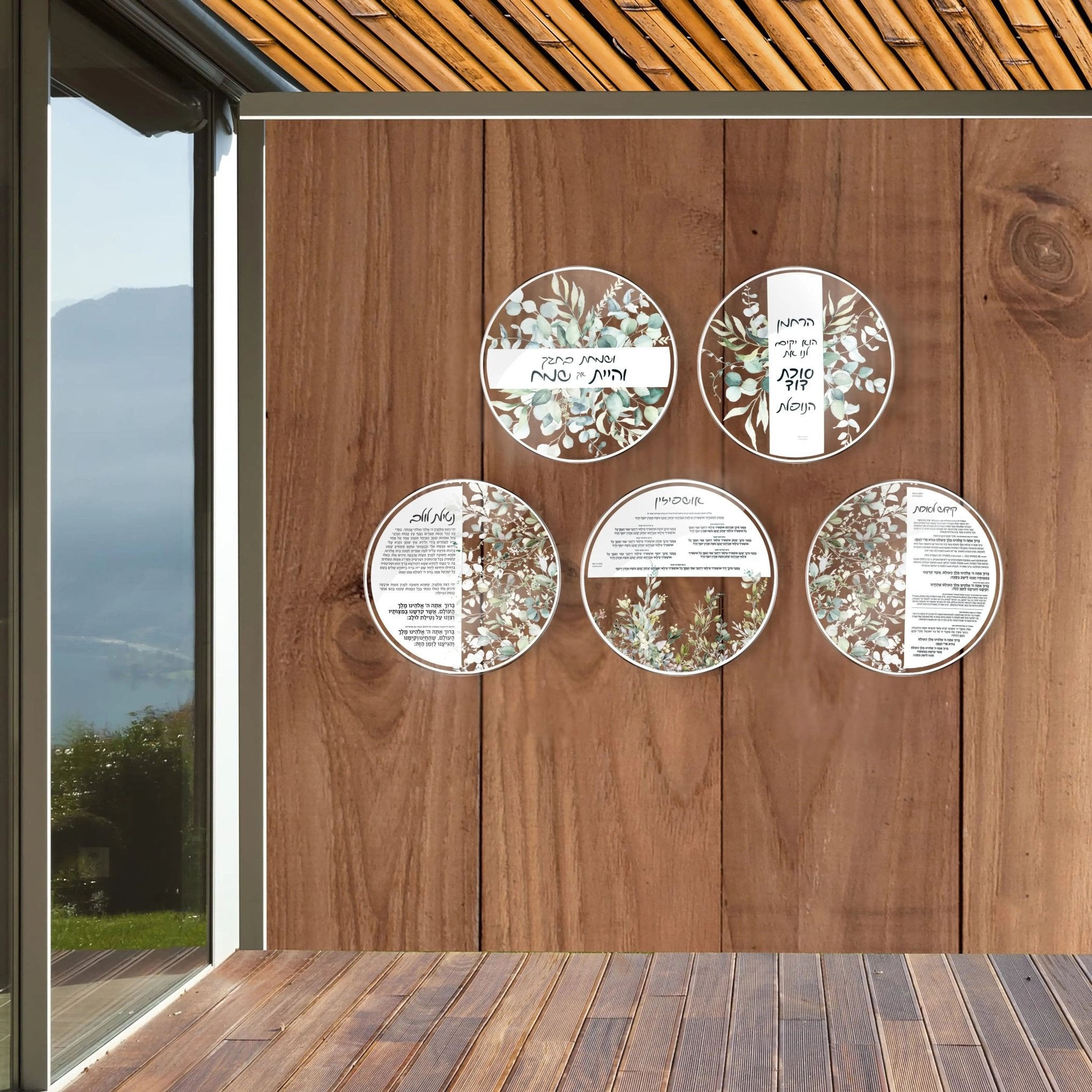 Five circular leaf sukkah decorations with painted details hung on wooden wall panel in modern sukkah space.