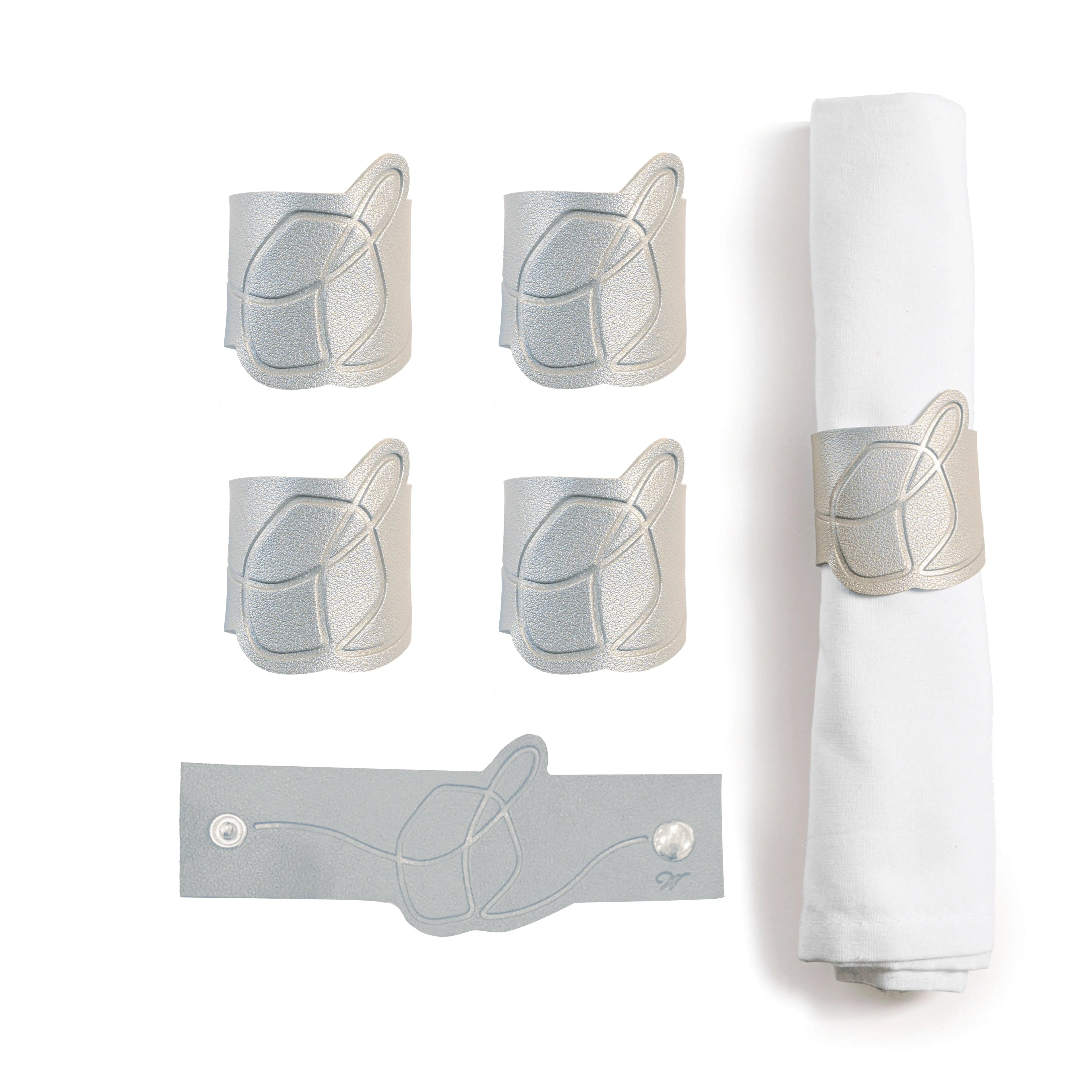 Set of five tan leather dreidel napkin rings with gray decorative holders displayed on white napkin, perfect for Chanukah table settings.