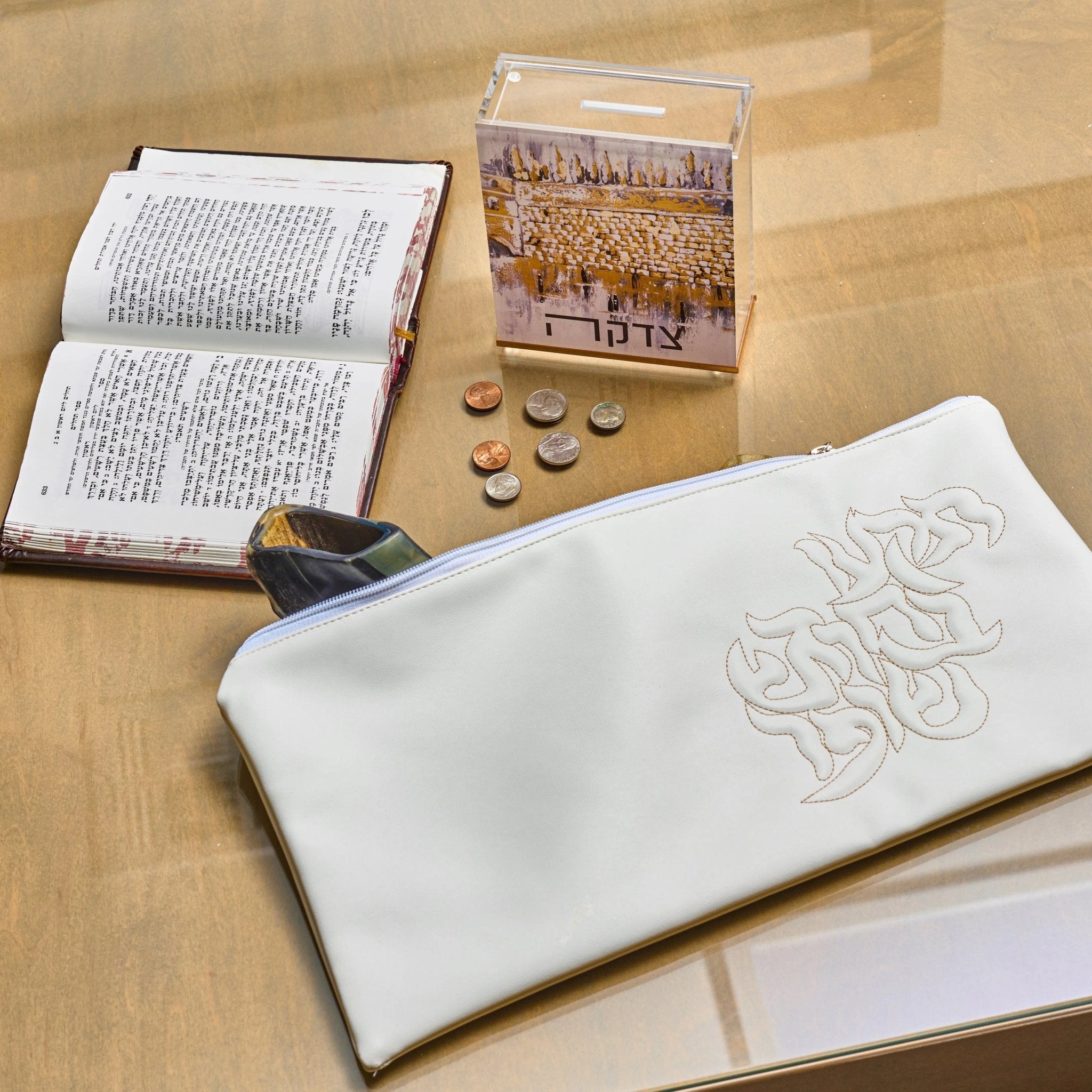 White leather pillow script shofar bag displayed on wooden surface with prayer book and holiday items nearby.