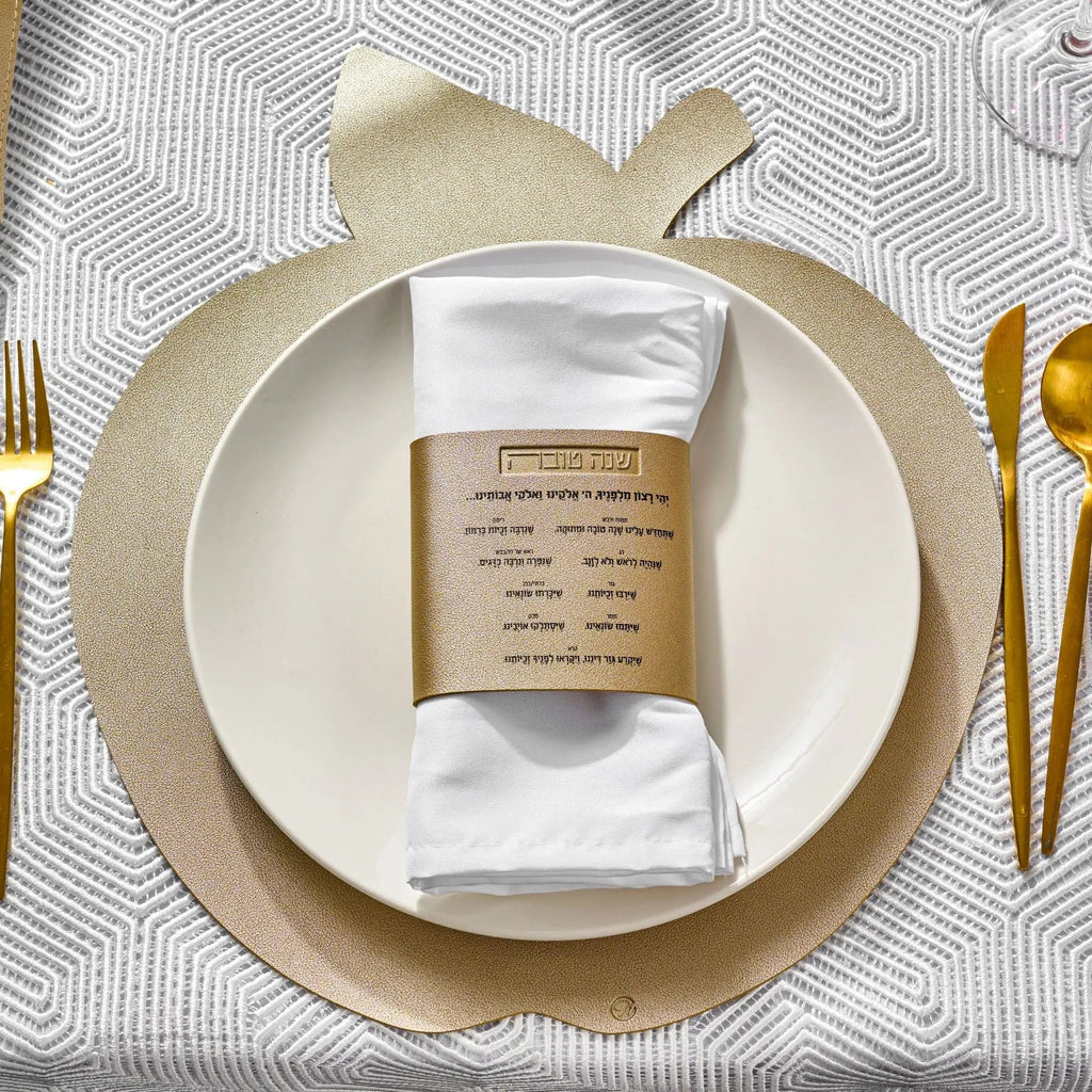 Gold leather simanim napkin wraps displayed on white plate with gold flatware at elegant table setting for holiday dinner
