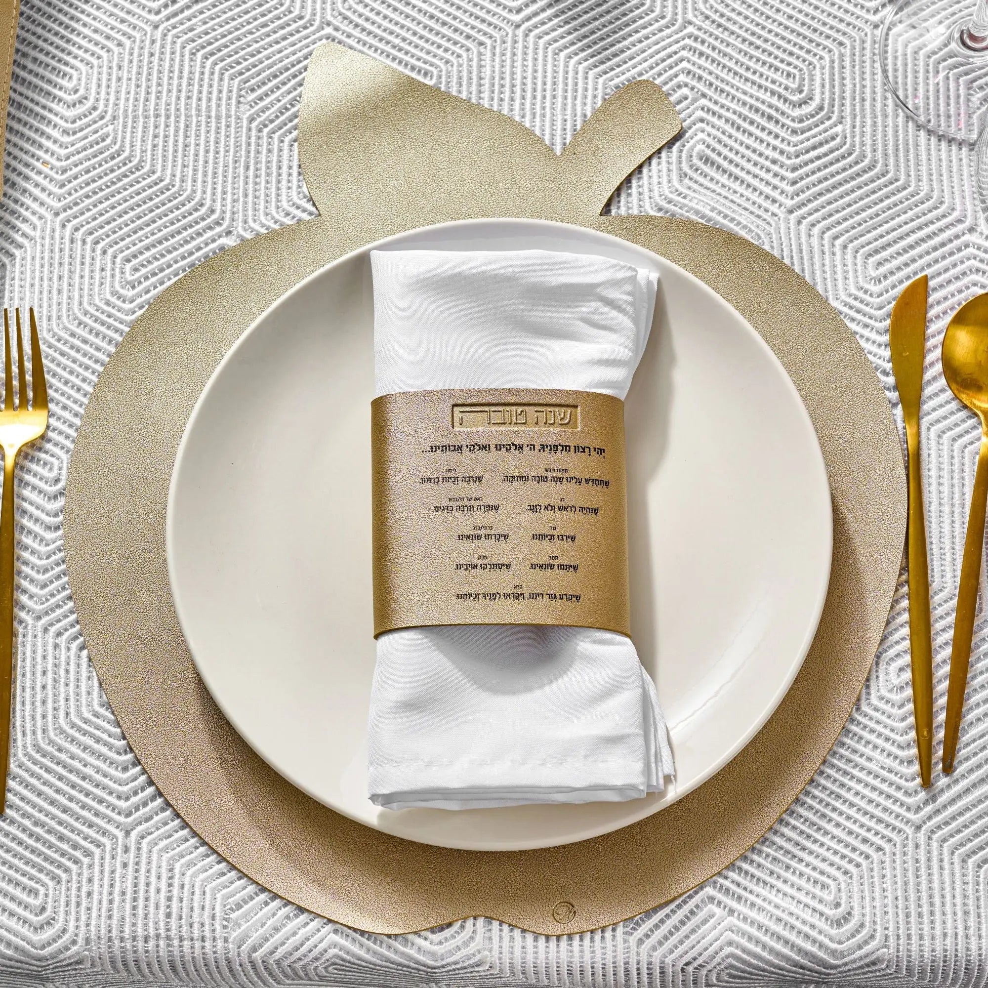 Gold leather simanim napkin wraps displayed on white plate with gold flatware at elegant table setting for holiday dinner