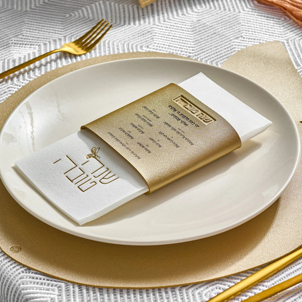 Gold leather Simanim napkin wrap holding a white napkin on a place setting with gold charger plate and cutlery.