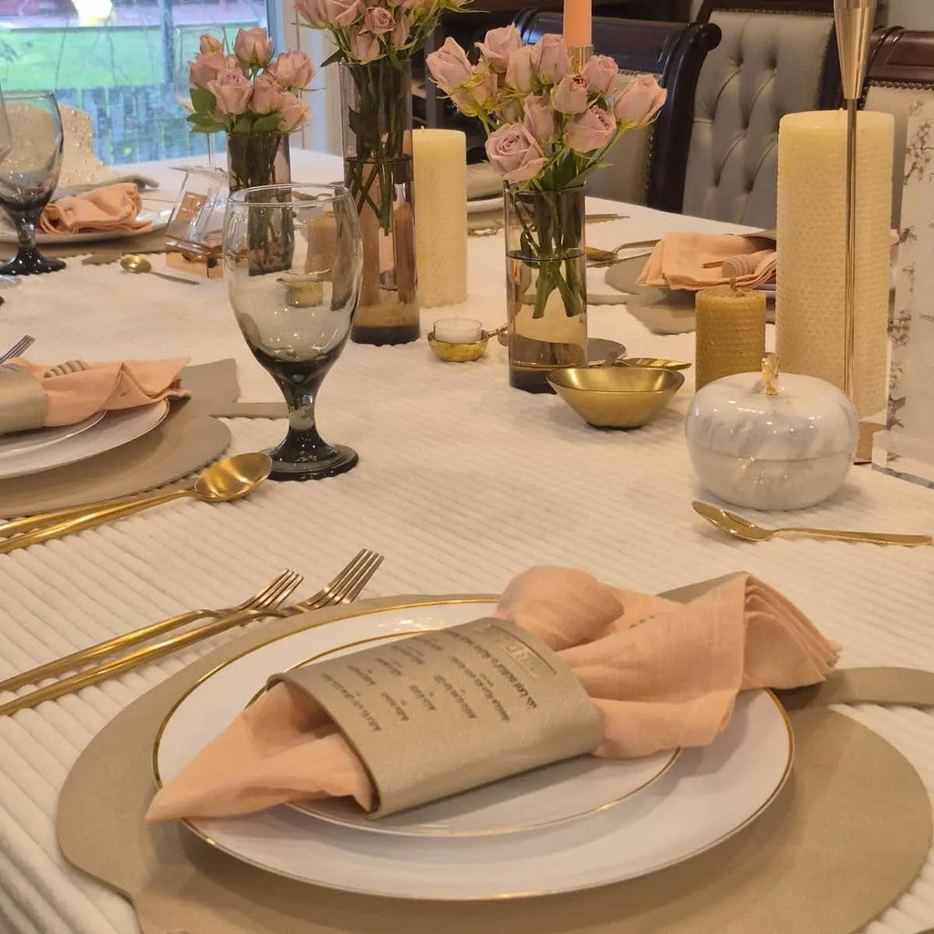 Tan leather Simanim napkin wrap holding a folded napkin on a white plate at a formal dinner table setting with gold accents