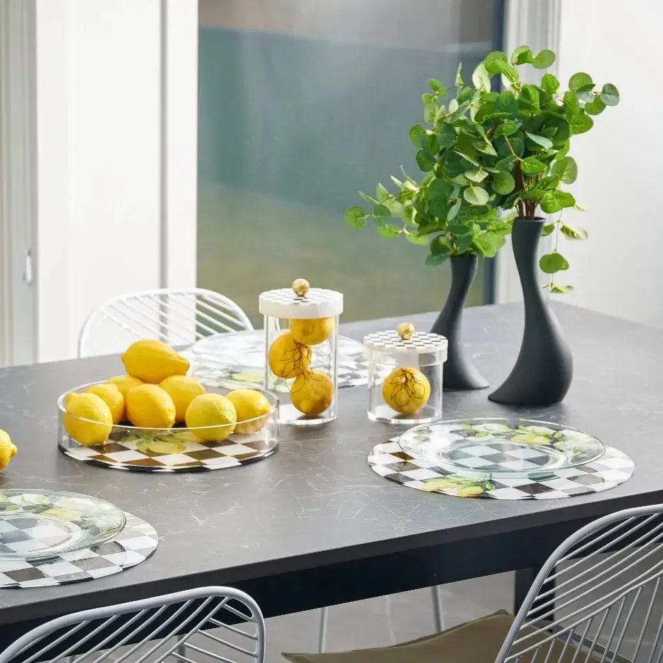 Lemona Chargers in black onyx with lemon pattern displayed on grey dining table with yellow lemons and green plant centerpiece