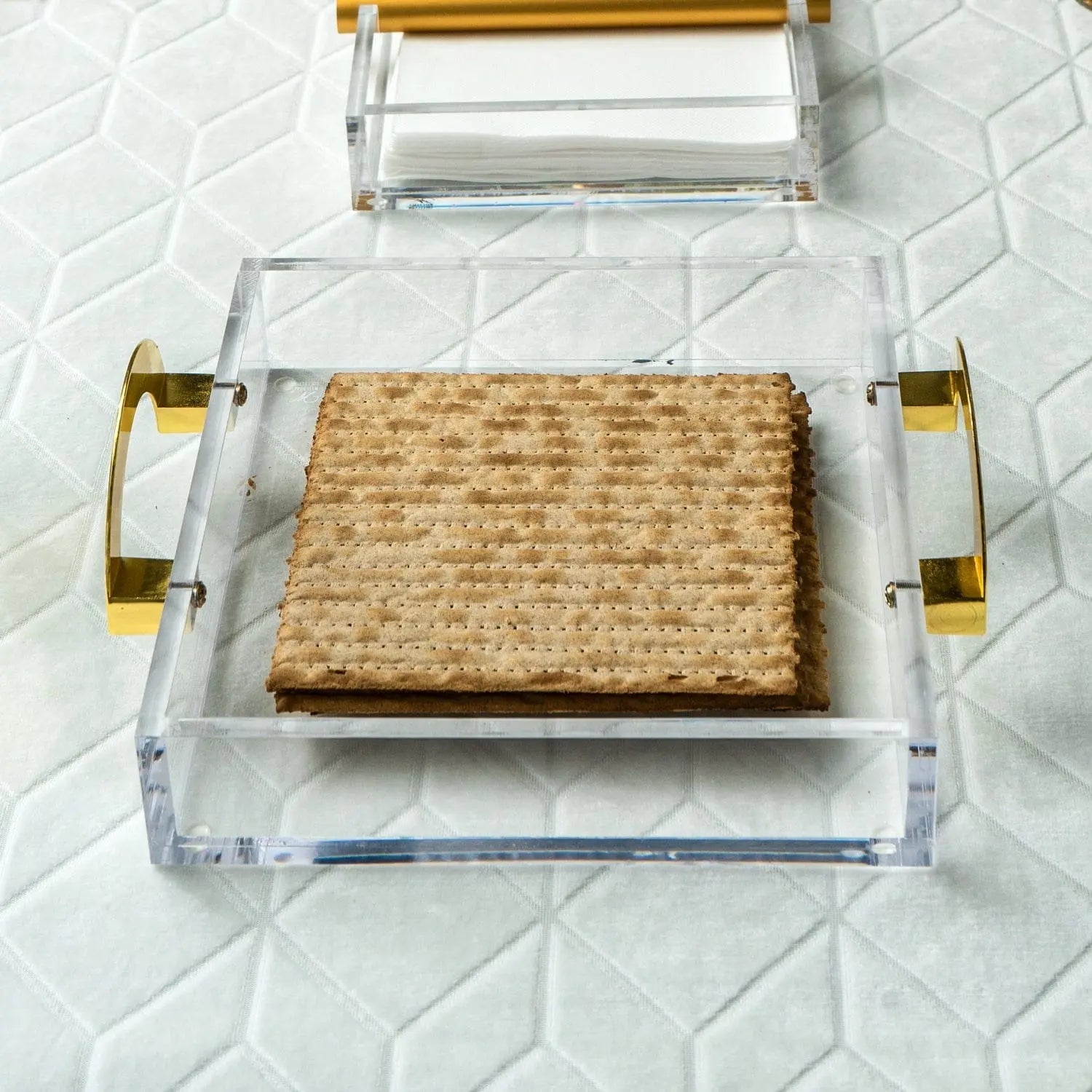 Clear lucite square tray with woven natural fiber insert and gold metal handles, perfect for Shabbat and Pesach entertaining.