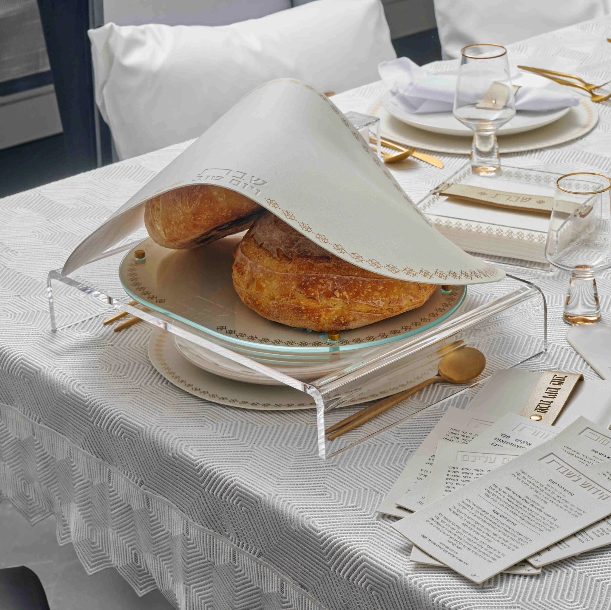 Marquesa Challah Cover in black leather with gold accents, displayed on a white table setting with place settings and bread during Shabbat dinner.