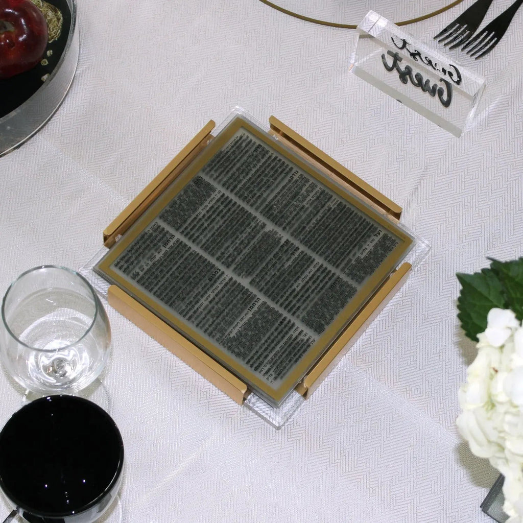 Gold and black MetaLucite layflat bencher set displayed on white linens with table settings, showing metallic frame design for Shabbat.