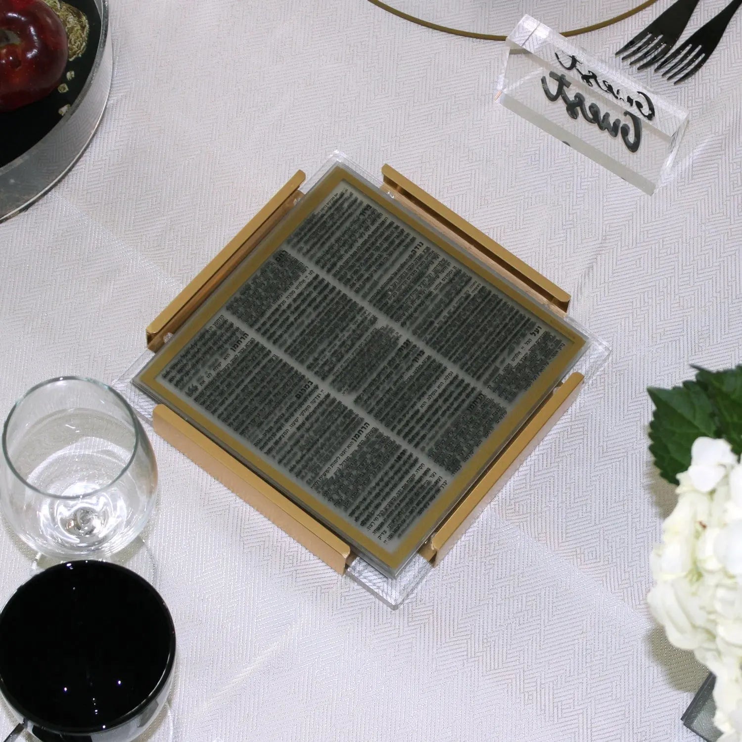 Gold and black MetaLucite layflat bencher set displayed on white linens with table settings, showing metallic frame design for Shabbat.