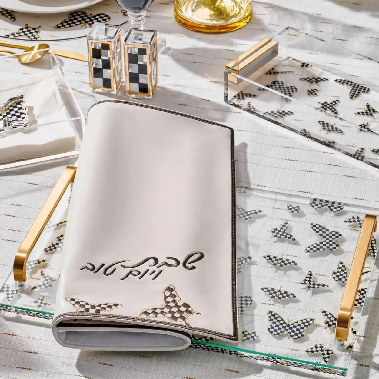 White challah cover with black Hebrew text and butterfly design on a decorative lucite butterfly tray with gold handles